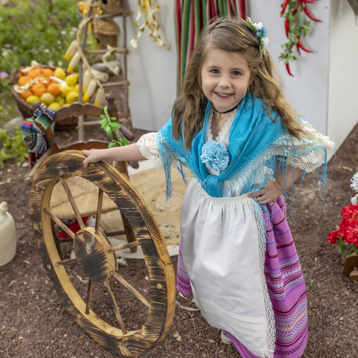 Niña de huertana con blusa azul junto al carro de frutas del decorado huertano de Murcia