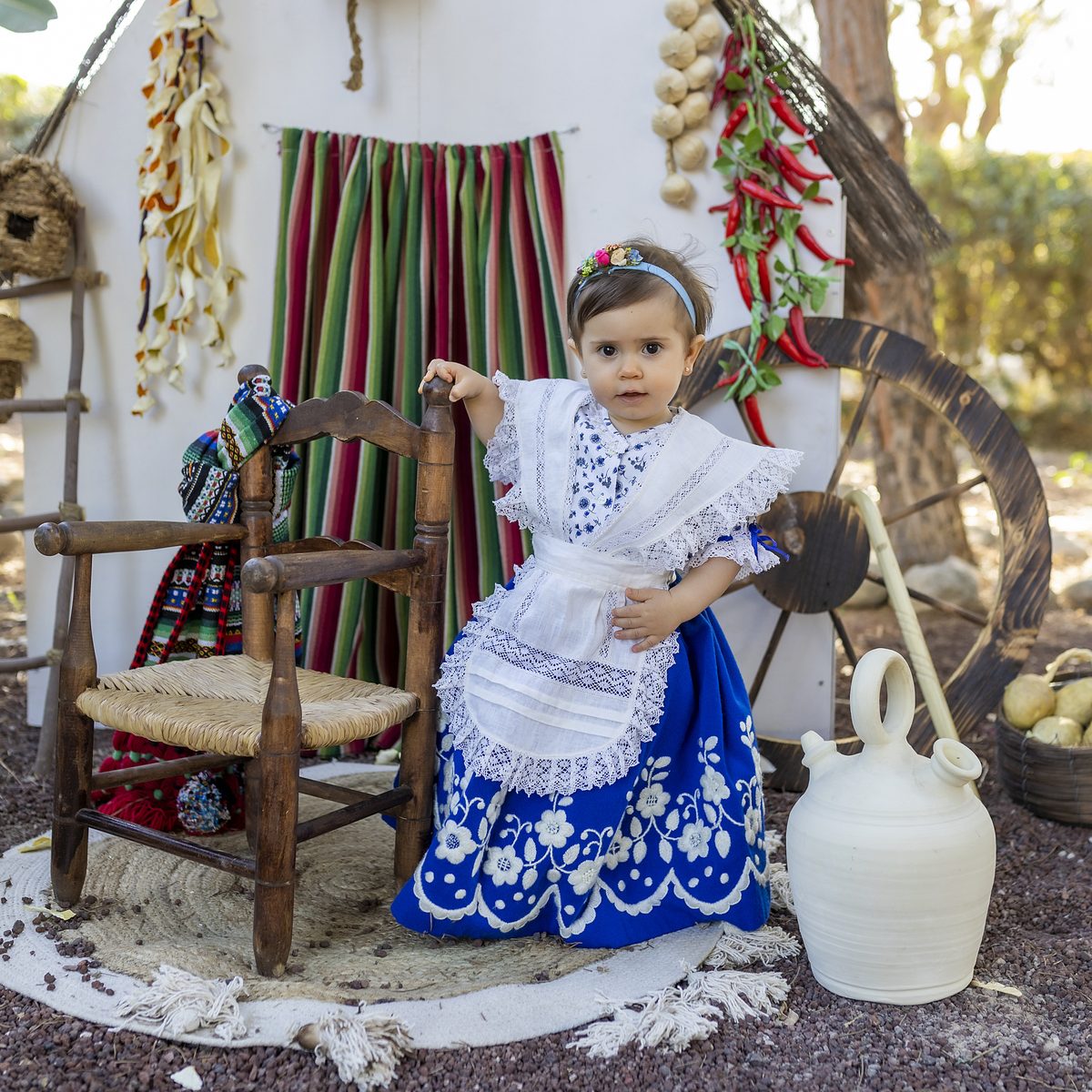 Niña de huertana sentada en una silla de enea en el decorado de la huerta de Murcia