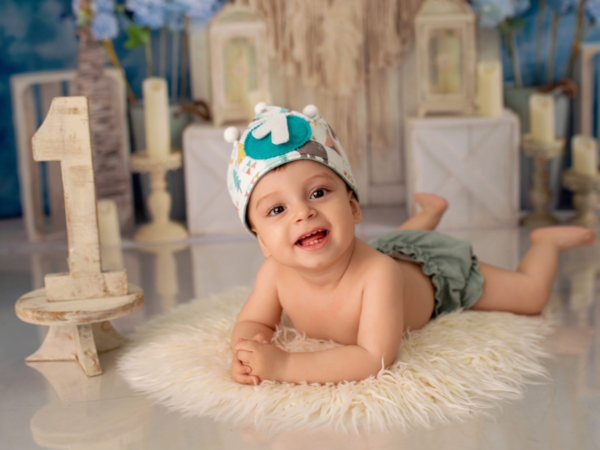 Bebé tumbado con gorro de fiesta en el decorado claro de la sesión smash cake en Murcia