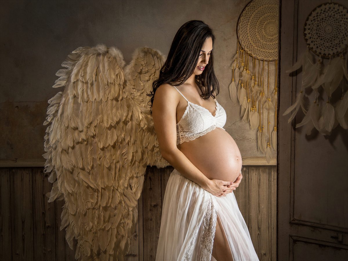 Embarazada con alas de plumas y vestido blanco en una sesión de maternidad en Murcia